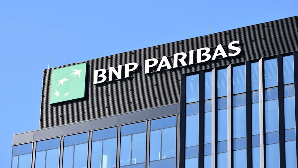 BNP Paribas corporate office building with logo and large sign on a glass facade against a blue sky.