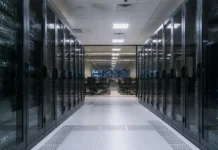 Creatio and Bayanat Expand AI Banking Automation in MENA Data center corridor flanked by glass-front server racks, leading to a control room with chairs and multiple screens at the far end.