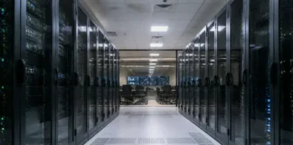 Creatio and Bayanat Expand AI Banking Automation in MENA Data center corridor flanked by glass-front server racks, leading to a control room with chairs and multiple screens at the far end.