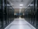Creatio and Bayanat Expand AI Banking Automation in MENA Data center corridor flanked by glass-front server racks, leading to a control room with chairs and multiple screens at the far end.