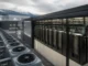 Blue Owl Leads $2.4 Billion AI Factory Financing for IREN Row of outdoor cooling units beside a data center server racks housed in a glass-enclosed enclosure, with mountains in the distance.