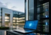 Munich Re Plans Cyber Insurance Acquisition of At-Bay Laptop showing a blue security shield screen beside a row of server racks outside a modern glass office building.